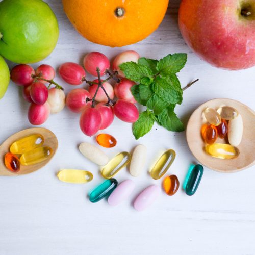 Multivitamin supplements from fruit on white wooden background